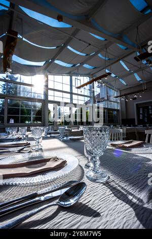 Vetro di cristallo sul tavolo in una luminosa sala banchetti con pareti in vetro. Foto scattate durante il giorno, con la luce del sole che scorre. Foto Stock