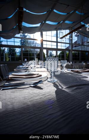 Vetro di cristallo sul tavolo in una luminosa sala banchetti con pareti in vetro. Foto scattate durante il giorno, con la luce del sole che scorre. Foto Stock