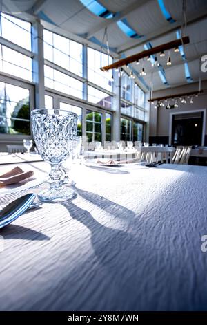 Vetro di cristallo sul tavolo in una luminosa sala banchetti con pareti in vetro. Foto scattate durante il giorno, con la luce del sole che scorre. Foto Stock