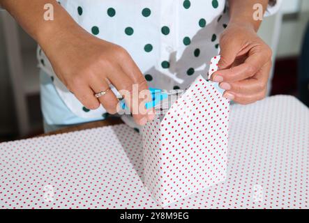 Primo piano di una persona che avvolge un regalo con carta a pois, usando le forbici. Cattura la gioia e la creatività dei regali e dei preparativi per le feste. Foto Stock