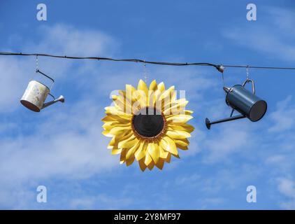 Deco da giardinaggio con lattine innaffianti e un girasole appeso sotto il cielo blu Foto Stock