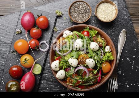 Lay piatto di insalata di verdure con mozzarella, lattuga, pomodori ciliegini, rafano, cetriolo, cipolla e basilico nel piatto di argilla Foto Stock