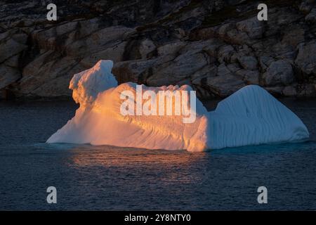 La luce del tramonto si riflette su un piccolo iceberg vicino a una costa rocciosa nell'Artico Groenlandia Foto Stock