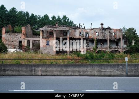 Facciata abbandonata di un grande edificio in mattoni e asfalto della strada davanti. Foto Stock