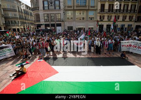 Malaga, Spagna. 6 ottobre 2024. I manifestanti tengono bandiere e cartelli dietro una grande bandiera palestinese durante una manifestazione globale contro il genocidio in Palestina. Un giorno prima dell'anniversario degli attentati del 7 ottobre e dell'inizio della guerra tra Israele e Hamas, migliaia di persone si recano per le strade della città di Malaga in solidarietà con il Libano e la Palestina per chiedere la fine del commercio di armi con Israele e dell'occupazione militare israeliana in Palestina. Credito: SOPA Images Limited/Alamy Live News Foto Stock