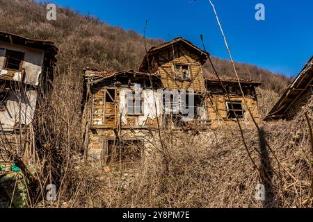 Case abbandonate e altri edifici, illuminati dalla luce del sole, vista sulla strada, villaggio di Pirin e montagna, Bulgaria Foto Stock