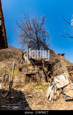 Case abbandonate e altri edifici, illuminati dalla luce del sole, vista sulla strada, villaggio di Pirin e montagna, Bulgaria Foto Stock