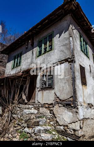 Case abbandonate e altri edifici, illuminati dalla luce del sole, vista sulla strada, villaggio di Pirin e montagna, Bulgaria Foto Stock