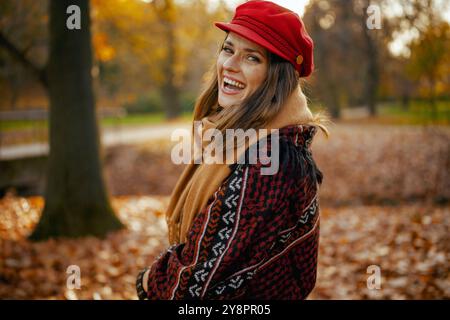 Ciao autunno. Ritratto di una donna felice ed elegante in cappello rosso con sciarpa nel parco cittadino. Foto Stock