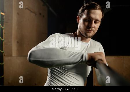 Ritratto medio di un forte sportivo che indossa una t-shirt a maniche lunghe per l'allenamento, preparando un bar alto per la pratica di spolverare attrezzature con gesso in palestra con illuminazione a basso volume, spazio per fotocopie Foto Stock