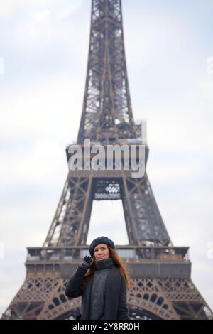 Donna parigina a Beret e cappotto grigio posa sull'autostrada con la Torre Eiffel Foto Stock