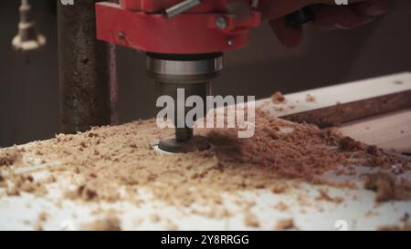 Fresatura del foro in legno. Lavoratore con fresa in azione. Punta da svasatura per svasare nel foro. Man utilizza una macchina perforatrice per realizzare un foro su W. Foto Stock