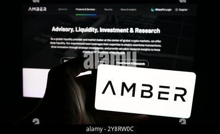 In questa immagine, una persona ha in mano un telefono cellulare con il logo della società di servizi crittografici Amber Global Limited davanti alla pagina Web aziendale. Foto Stock