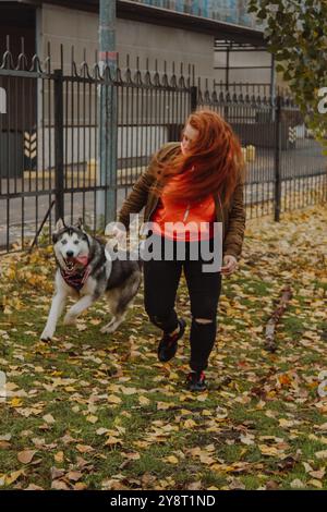 Una giovane ragazza con lunghi capelli rossi gioca con un cane husky. Il processo di integrazione dell'individuo nel sistema sociale. Una donna fa entrare il suo cane Foto Stock