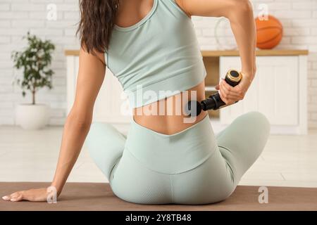 Giovane donna sportiva che utilizza un dispositivo di massaggio percussivo dopo l'allenamento in palestra Foto Stock