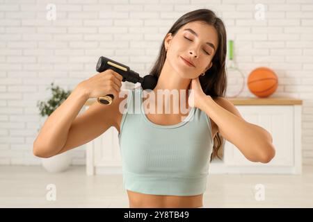 Giovane donna sportiva che utilizza un dispositivo di massaggio percussivo dopo l'allenamento in palestra Foto Stock