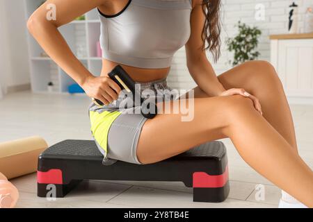 Giovane donna sportiva che utilizza un dispositivo di massaggio percussivo dopo l'allenamento in palestra Foto Stock