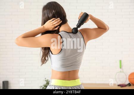 Giovane donna sportiva che utilizza un dispositivo di massaggio percussivo dopo l'allenamento in palestra Foto Stock