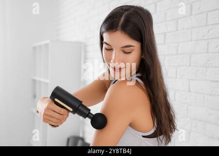 Giovane donna sportiva che utilizza un dispositivo di massaggio percussivo dopo l'allenamento in palestra Foto Stock