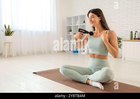 Giovane donna sportiva che utilizza un dispositivo di massaggio percussivo dopo l'allenamento in palestra Foto Stock