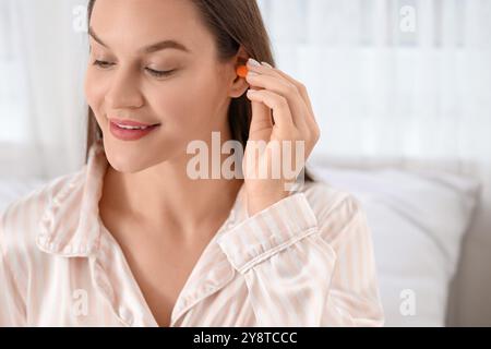 Giovane donna che mette il tappo dell'orecchio in camera da letto, primo piano Foto Stock