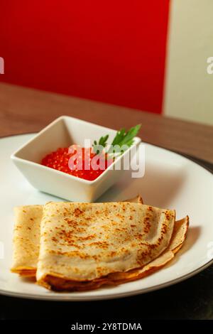 Pancake russi tradizionali con caviale rosso e prezzemolo su piatto bianco Foto Stock