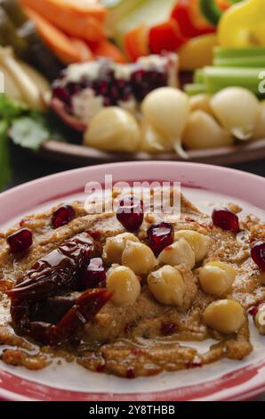 Vista dall'angolo basso sul piatto di hummus vegetale con pomodoro essiccato al sole e ricoperto di ceci e olio d'oliva Foto Stock