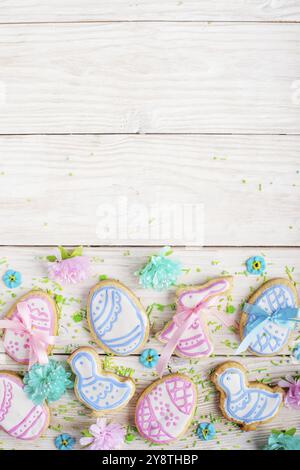 Spolverini di zucchero e biscotti frostati di Pasqua a forma di pollo all'uovo e coniglio su sfondo bianco tavolo di legno. Mockup verticale piatto con copia spa Foto Stock