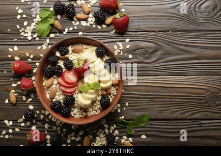 Appartamento laici vista superiore a frutto sano muesli con banana fragola mandorle e blackberry nel piatto di argilla su legno tavolo da cucina Foto Stock