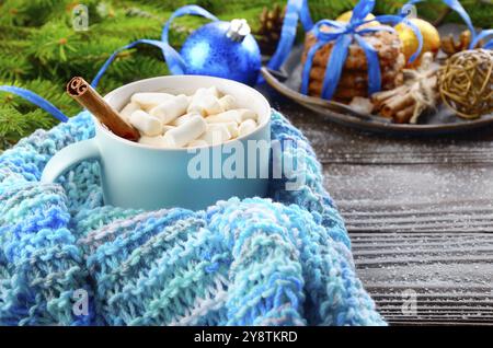 Natale sfondo blu di cioccolata calda tazza con marshmallows in maglia Sciarpa, ramo di abete e il vassoio con gingerbread cookie sul tavolo di legno Foto Stock