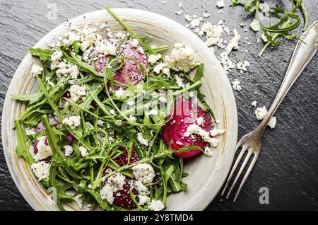 Vista da sopra al piatto di argilla con barbabietole rosse foglie di rucola e formaggio feta insalata su pietra ardesia vassoio closeup vista. Forcella a parte Foto Stock