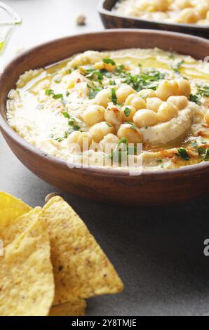 Vista sul closeup all'Hummus sormontato da olio di oliva di fagioli e foglie di coriandolo verde sul tavolo da cucina con tortilla patatine Foto Stock