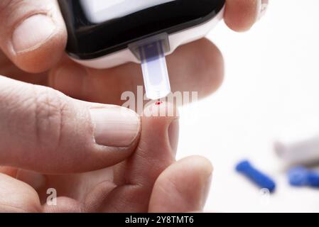 Dita caucasiche con gocce di sangue pronte per il test del glucosio a domicilio con vista ravvicinata del glucometro. Concetto di consapevolezza del diabete Foto Stock