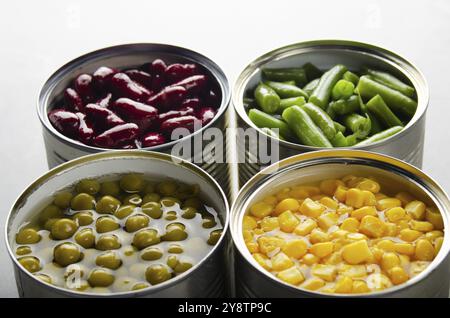 Fagioli, fagioli verdi, piselli e mais in lattine aperte su tavola da cucina. Fondo di alimenti non deperibili Foto Stock