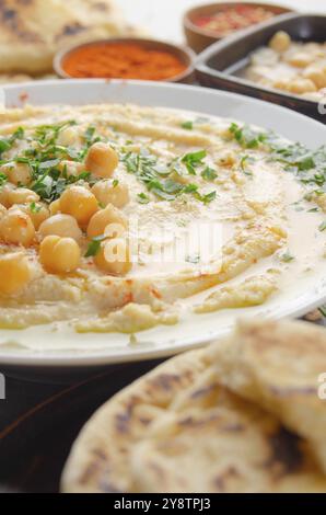 Vista sul closeup all'Hummus sormontato da olio di oliva di fagioli e foglie di coriandolo verde sul tavolo da cucina con pane pita Foto Stock