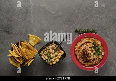 Hummus piatto con pomodori secchi in piatto di argilla con ceci e foglie di coriandolo verde su tavola di pietra servita con patatine di tortilla Foto Stock