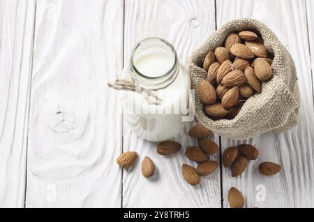 Latte o yogurt in una bottiglia di vetro bianco sul tavolo di legno con le mandorle nel sacco di canapa a parte Foto Stock