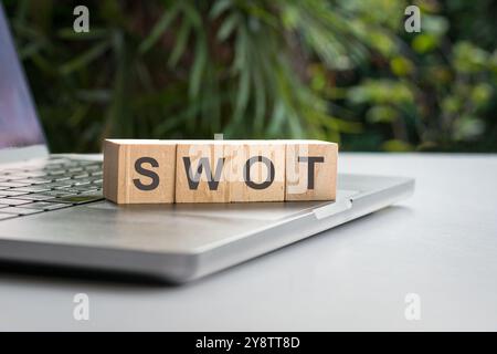 SWOT, parola scritta su un blocco di legno quadrato, sulla parte superiore del computer portatile. Foto Stock