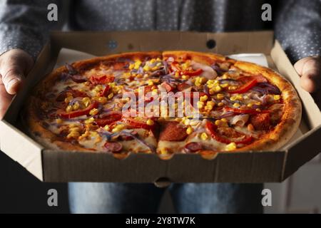 Le mani maschili caucasiche trattengono un'ampia scatola di cartone aperta con pizza al peperoni e vista frontale con granturco dolce Foto Stock