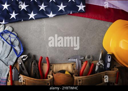 Attrezzi hardhat toolbelt e noi bandiera su cemento cemento sfondo del banner del giorno di lavoro mockup Foto Stock