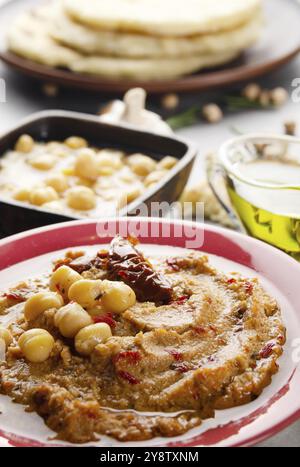 Hummus fresco fatto in casa in piatto di argilla condito con olio d'oliva, ceci, spezie e pomodori secchi al sole su tavola di pietra Foto Stock