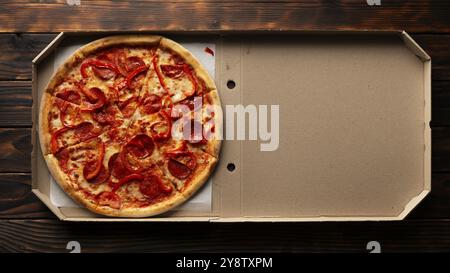 Pizza al peperone con peperoni in scatola di cartone aperta su un tavolo di legno scuro piatto con spazio per le copie Foto Stock