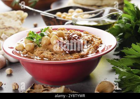 Vista a basso angolo a Hummus sormontato da ceci, foglie di coriandolo verde olio d'oliva e pomodori secchi al sole su tavola di pietra con pane pita da parte Foto Stock