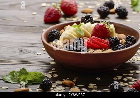 Frutto sano muesli con banana fragola mandorle e blackberry nel piatto di argilla su legno tavolo da cucina Foto Stock