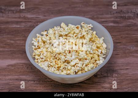 Una ciotola di popcorn è seduta su un tavolo di legno. Il cassone è riempito di popcorn e viene posizionato sulla barra. Foto Stock