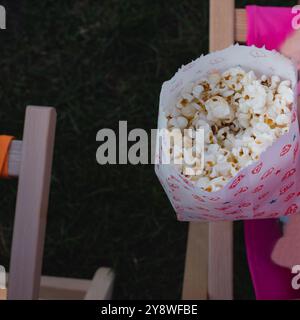 Una persona tiene in mano un sacchetto di popcorn. La borsa è rossa e bianca e presenta un design a fumetti. Foto Stock