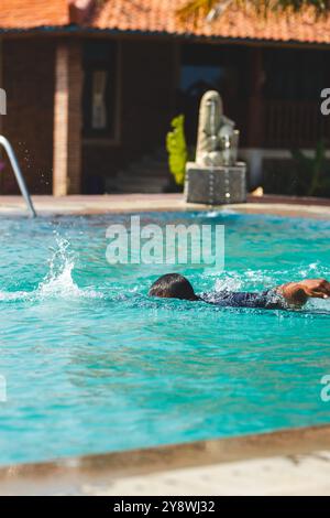 Uomo che nuota in stile libero nella scintillante piscina. Vivace piscina estiva con acque blu cristalline. Foto Stock