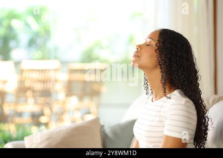 Vista laterale ritratto di una donna nera che respira aria fresca seduto su un divano di casa Foto Stock