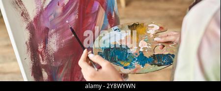 Una giovane donna ama esprimere la sua creatività dipingendo a casa, lavorando intensamente sulle sue opere d'arte. Foto Stock