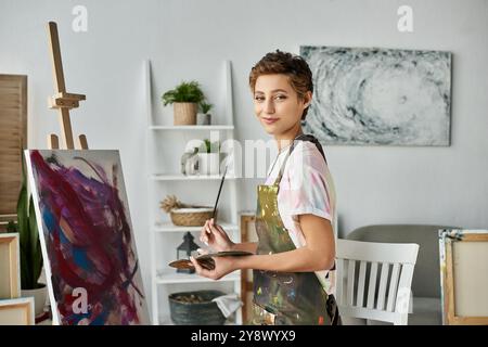 In un allegro studio casalingo, una giovane donna con i capelli corti ama dipingere, circondata dalla creatività e dai colori. Foto Stock